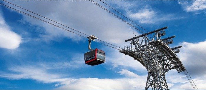 LEITNER gondola cabin passing a lattice ropeway tower against a blue sky