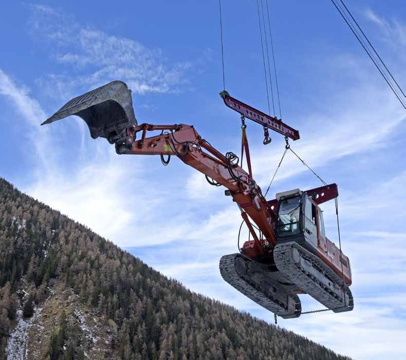 SEIK cable crane lifting an excavator across a forested mountain slope